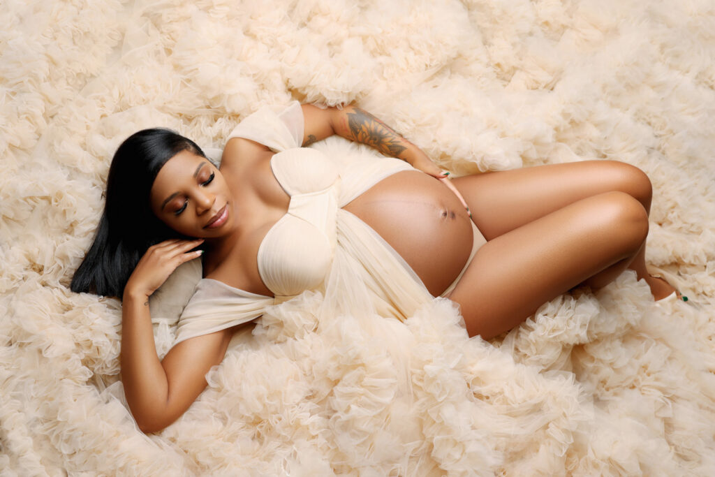 Pregnant mom connecting with her baby while posing laying down on her back in a beautiful tulle flowy maternity couture gown.